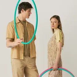 Een man en een vrouw staan en houden kleurrijke hoelahoepringen vast; hij houdt een turquoise ring vlakbij zijn gezicht, zij houdt twee ringen naast zich vast.