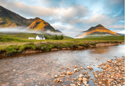 A tranquil landscape featuring a river, a white house, and mountains under a cloudy sky.