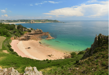A scenic view of a sandy beach surrounded by cliffs and lush greenery, with clear blue waters.