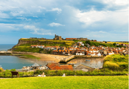 A scenic view of a coastal village with colourful houses, cliffs, and a castle overlooking the sea.