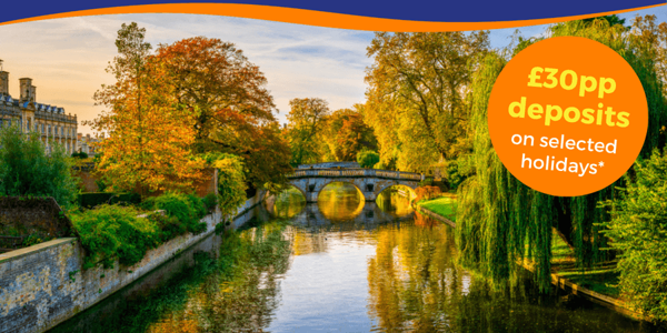 A scenic view of a river with a stone bridge, surrounded by autumn foliage and historic buildings.