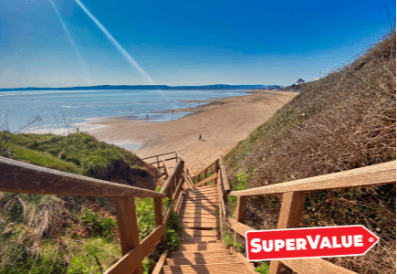 Wooden steps leading down to a sandy beach with calm water and a clear blue sky.