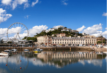 A scenic view of a coastal town with a ferris wheel, boats, and reflections in the water.