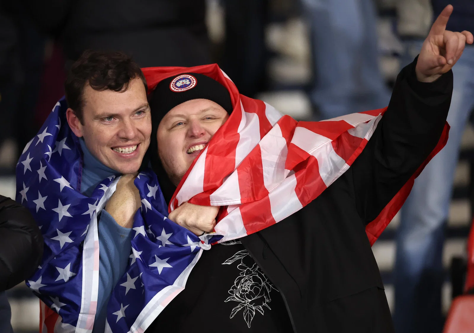 A pair of World Cup fans wrapped in an American flag with big smiles.