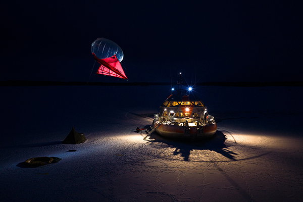 The lights of the Tara research vessel shine in the darkness as it deploys a research balloon.