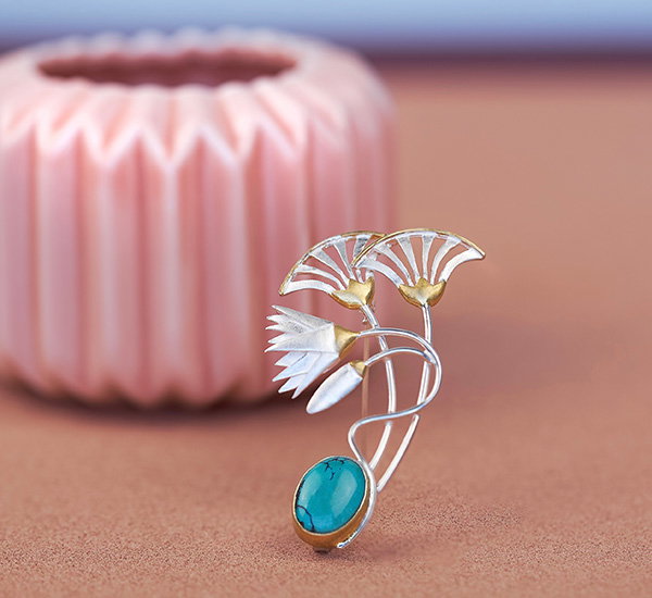 Silver brooch featuring an elaborate lotus flower design, set against a ceramic shape and pastel background. - Shop Now.