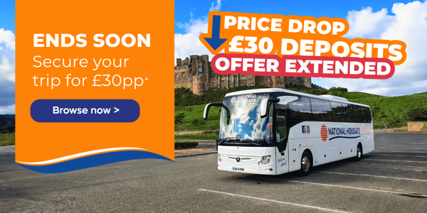A coach from National Holidays parked near a historic castle under a blue sky with clouds.