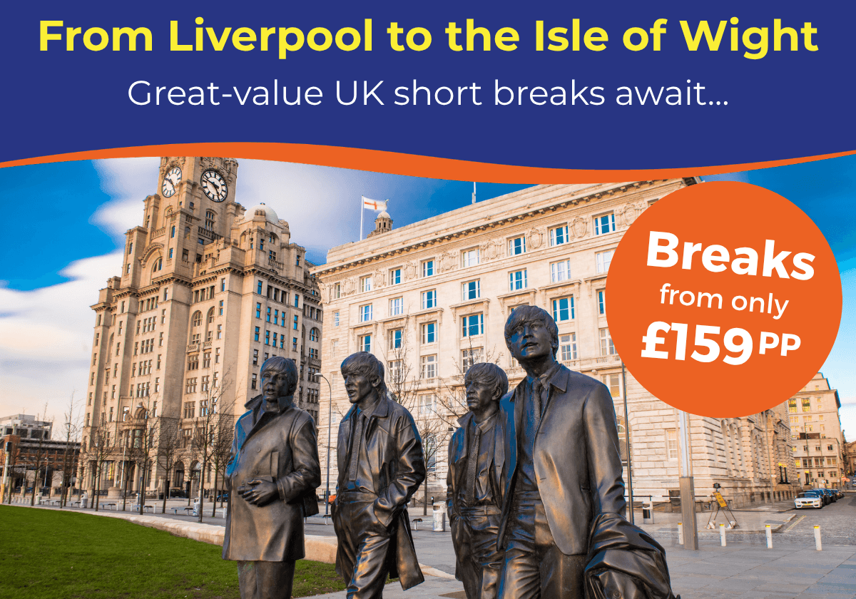 Statues of four musicians stand in front of historic buildings in Liverpool, under a blue sky.