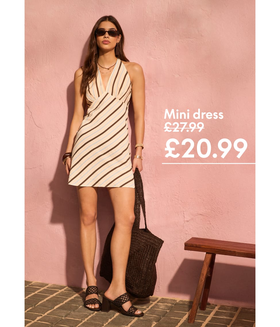 Model wearing a gold crochet strapless maxi dress stands barefoot beside a palm tree on a sandy tropical beach. Surrounded by lush greenery and sunshine, she styles the look with sunglasses and metallic sandals for a chic holiday outfit.