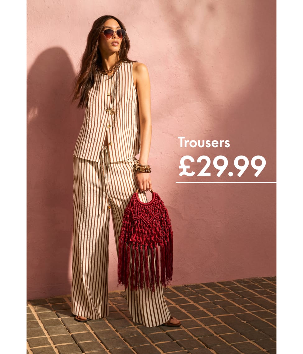 Model wears a green tropical-print maxi dress with a palm and floral pattern, styled with flat sandals, sunglasses and a woven tote bag. The image features two views of the outfit alongside the headline “Paradise Prints” and copy celebrating bold holiday-ready prints inspired by island landscapes.