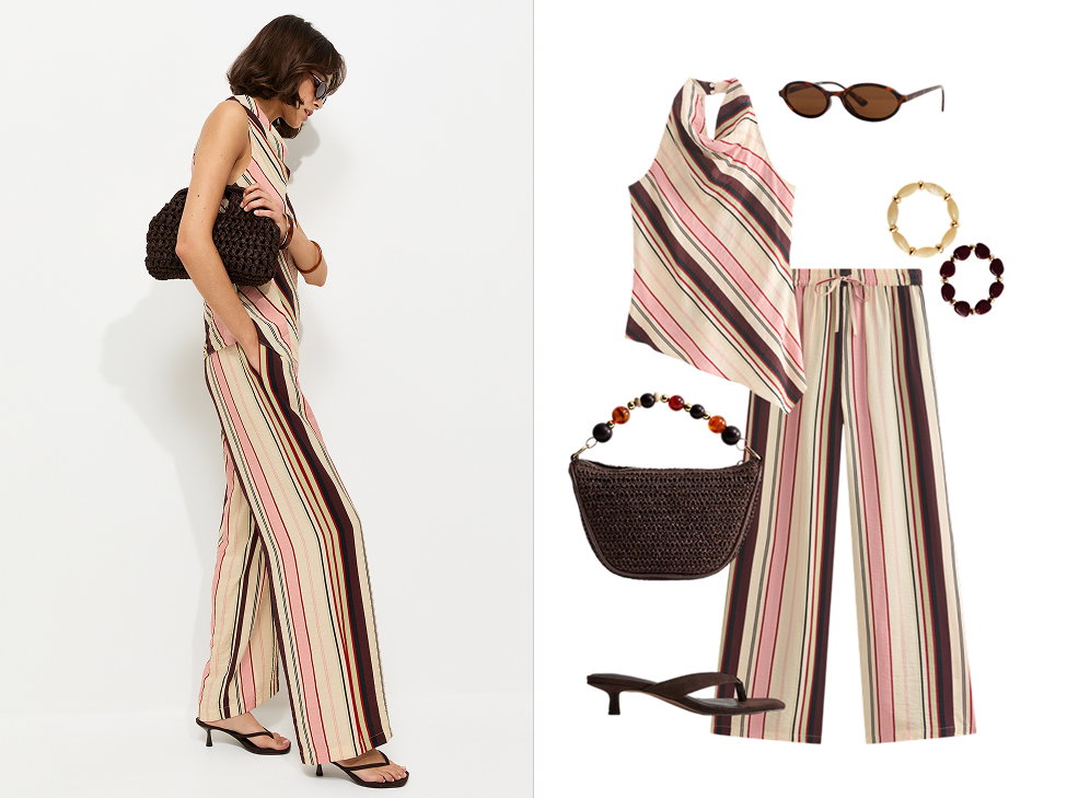 Model wearing a flowing cream maxi dress walks across a sunlit tropical beach surrounded by palm trees and exotic plants. Styled with sunglasses, layered jewellery and metallic sandals, the look creates an effortless holiday-ready outfit.