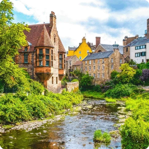 Image Description: A stream surrounded by green grass leading to a village with brick buildings and houses.