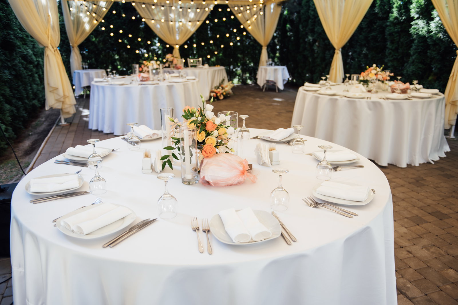 Outdoor wedding table with white linens, peach florals and pillar candles