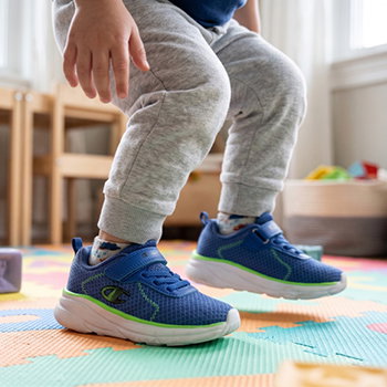 Toddler's legs and feet wearing blue mesh trainers with green trim standing on a colourful foam play mat in a bright playroom