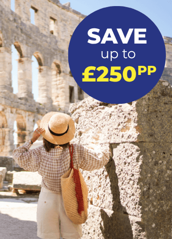 A person in a straw hat stands in a historic stone structure, looking back at the ruins.