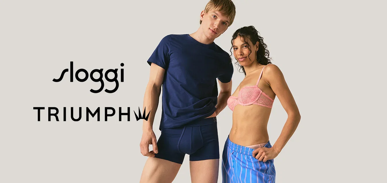 Ein Mann in einem marineblauen T-Shirt und Boxershorts steht neben einer Frau in einem pinken BH und blau gestreiften Shorts vor einem schlichten Hintergrund.