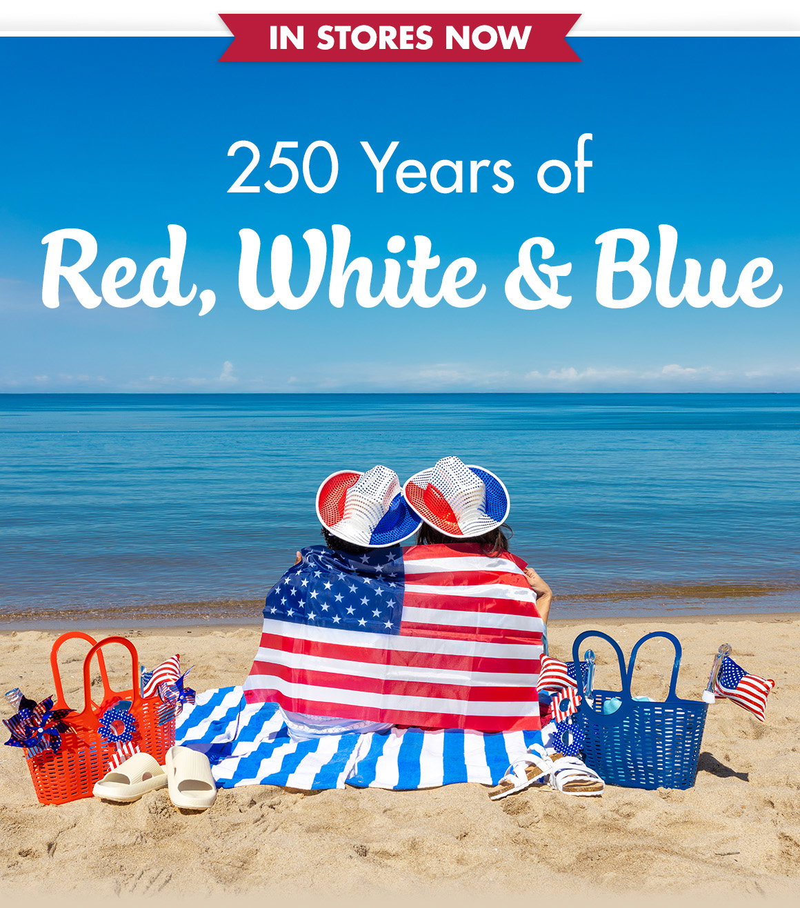 250 years of Red, White and Blue. Image of two friends sitting on a beach looking at the ocean wrapped in an American flag.