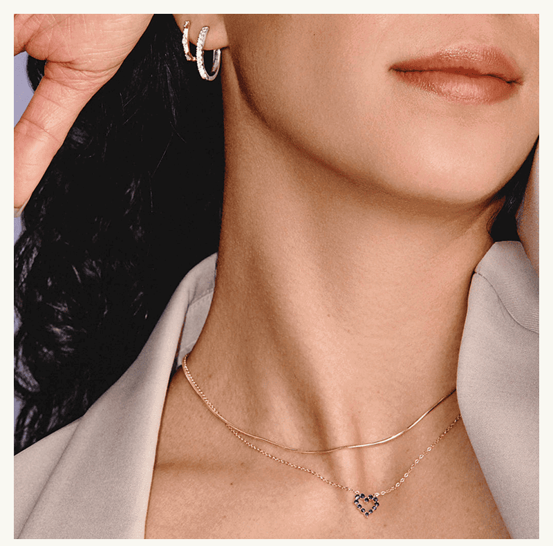 A model wearing two diamond hoop earrings, a gold necklace and a gemstone heart pendant.