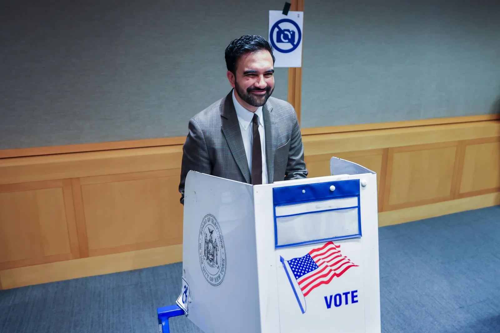 New York Mayor Zohran Mamdani smiling from behind a voting screen.