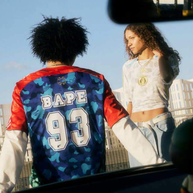 Male model standing with his back to the camera wearing the Home jersey, while a female model wearing the Away jersey looks toward him.