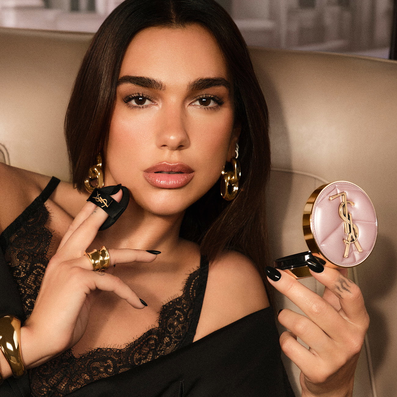 Singer Dua Lipa applying makeup while holding a luxury YSL cushion foundation compact in a quilted pale pink case.
