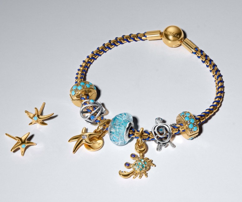 A Pandora ME bracelet with colourful sea charms and studs on a grey background.