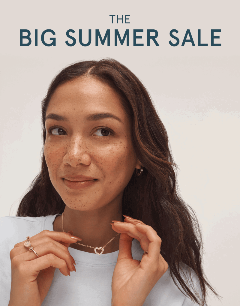 Female model showcasing yellow gold rings, earrings, and a heart-shaped necklace. The big summer sale.
