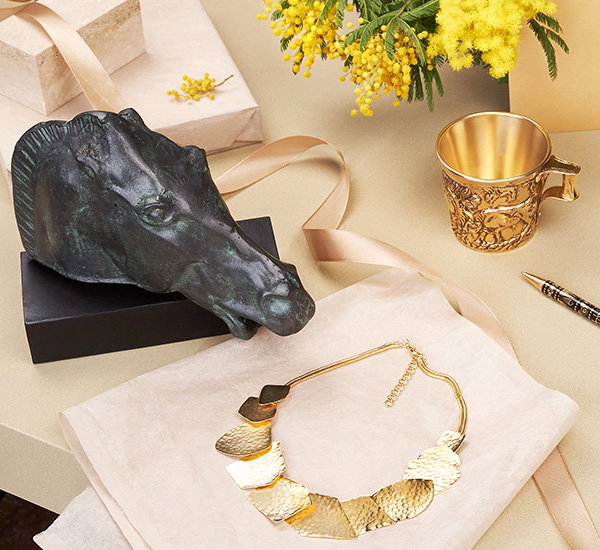 Museum-inspired gifts including a bronze Horse of Selene replica, gold-plated hammered necklace and Vapheio Cups replica on a neutral background with ribbons and flowers. - Gifts Collection.