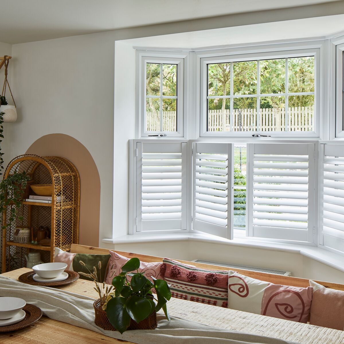 White shutters installed on a three-panel bay window in a dining area 