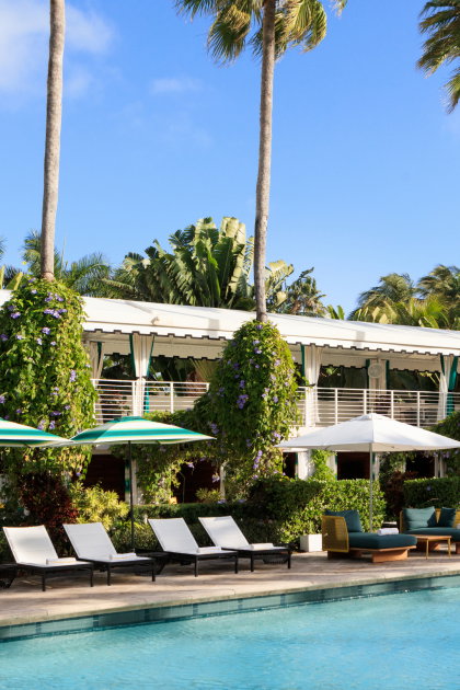 Beneath a clear blue sky, a bright and inviting pool is surrounded by sleek lounge chairs and teal-striped umbrellas.
