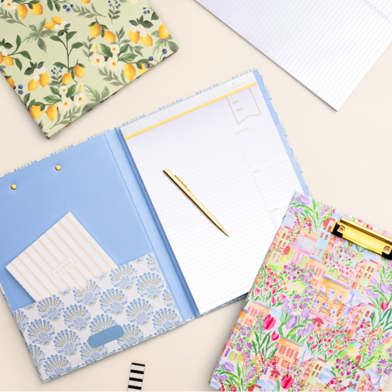open and closed clipfolios, notebook, gold pen, beige background