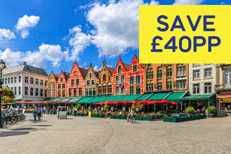 Colourful historic buildings line a cobblestone square, with outdoor dining areas and blue skies.