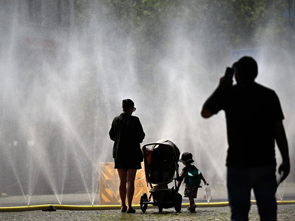 People stand near water hoses spraying mist to provide relief from summer heat as part of Cologne, Germany’s climate adaptation efforts.
