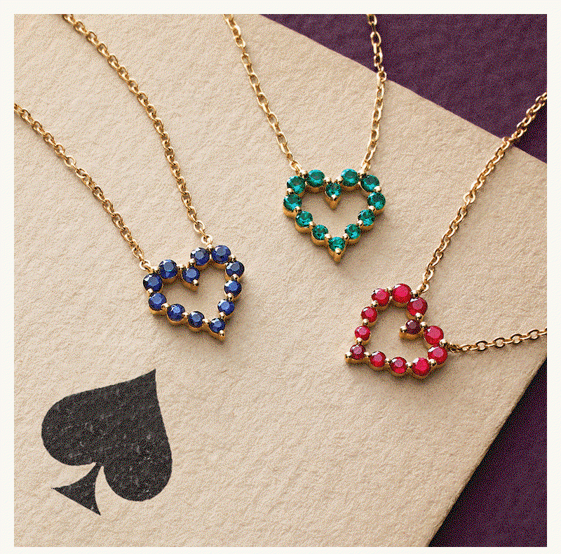 Gold chains with open-heart shaped red, green & blue gemstone pendants, on top of playing card.