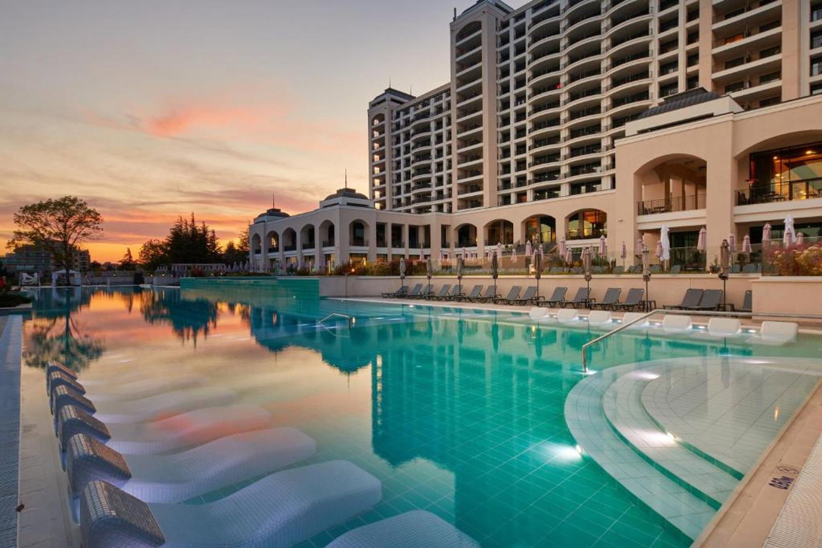 Resort hotel with large turquoise outdoor pool, submerged loungers and multi-storey balconies at sunset