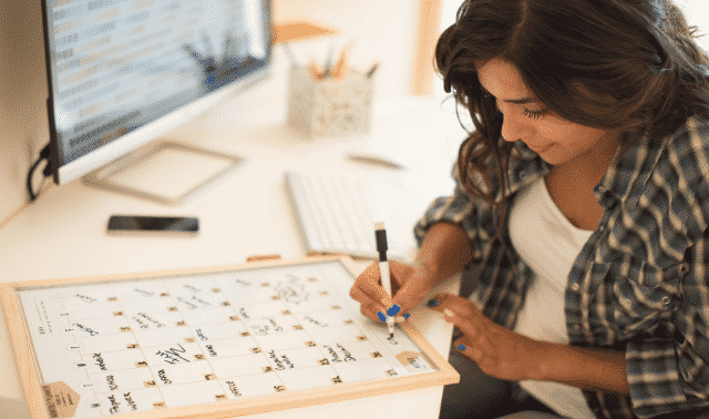 Woman using a wipe-off calendar to write down 30 family history writing tips.