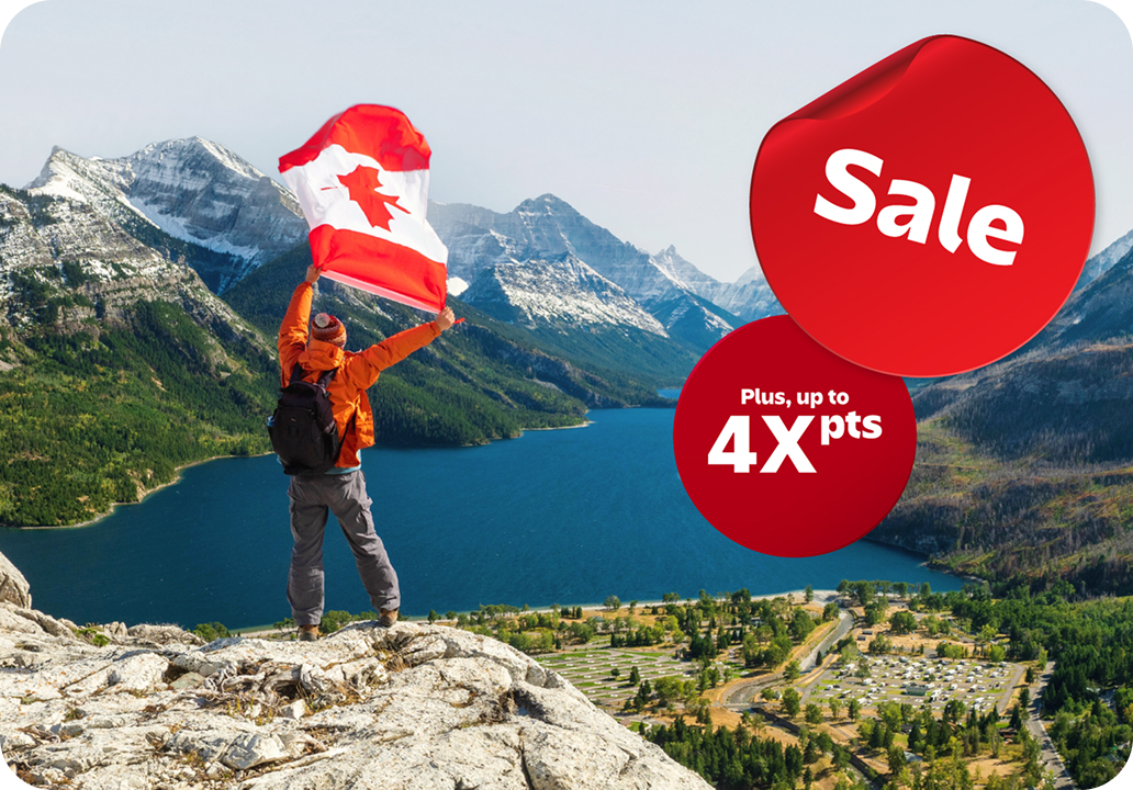 A hiker waving a Canadian flag on a rocky summit overlooking a mountain lake