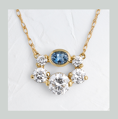 A 14k yellow gold Hemline Necklace in Blue Montana Sapphire shown on a textured white background.