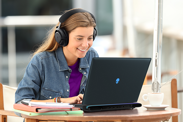 Happy student listening a video tutorial on line with a laptop sitting in a bar terrace