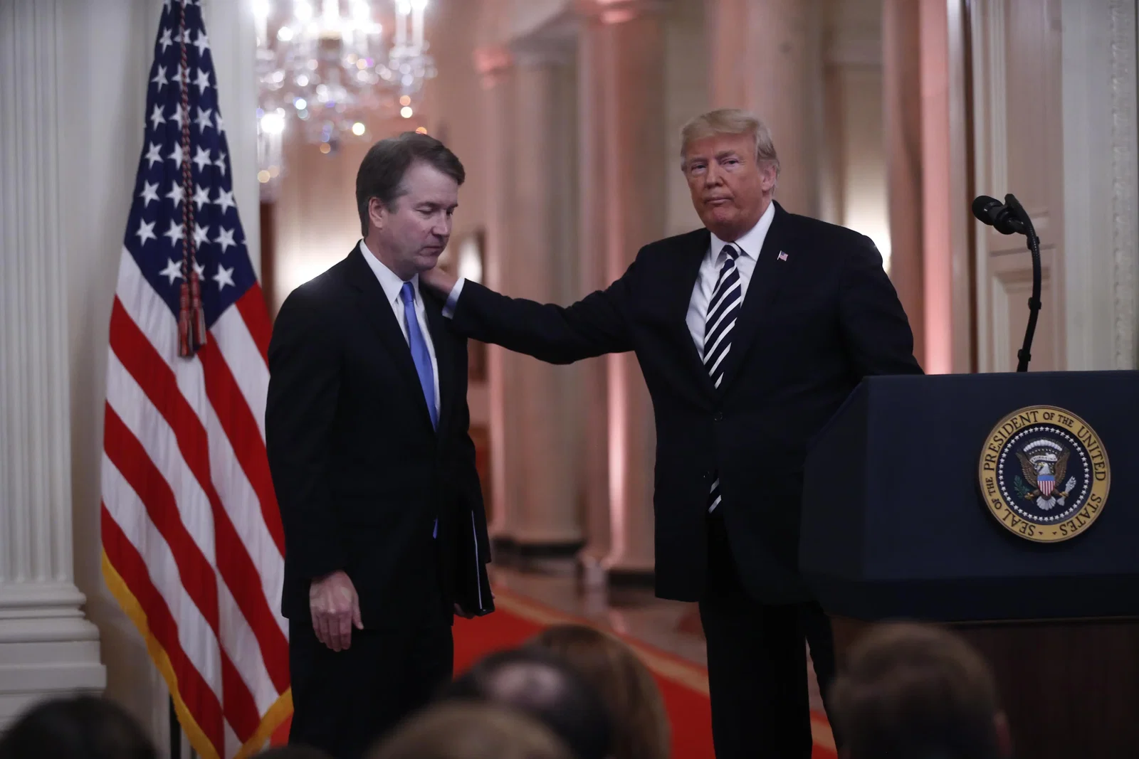 President Donald Trump places and hand on Justice Brett Kavanaugh's shoulder, as both stand in a White House hallway.