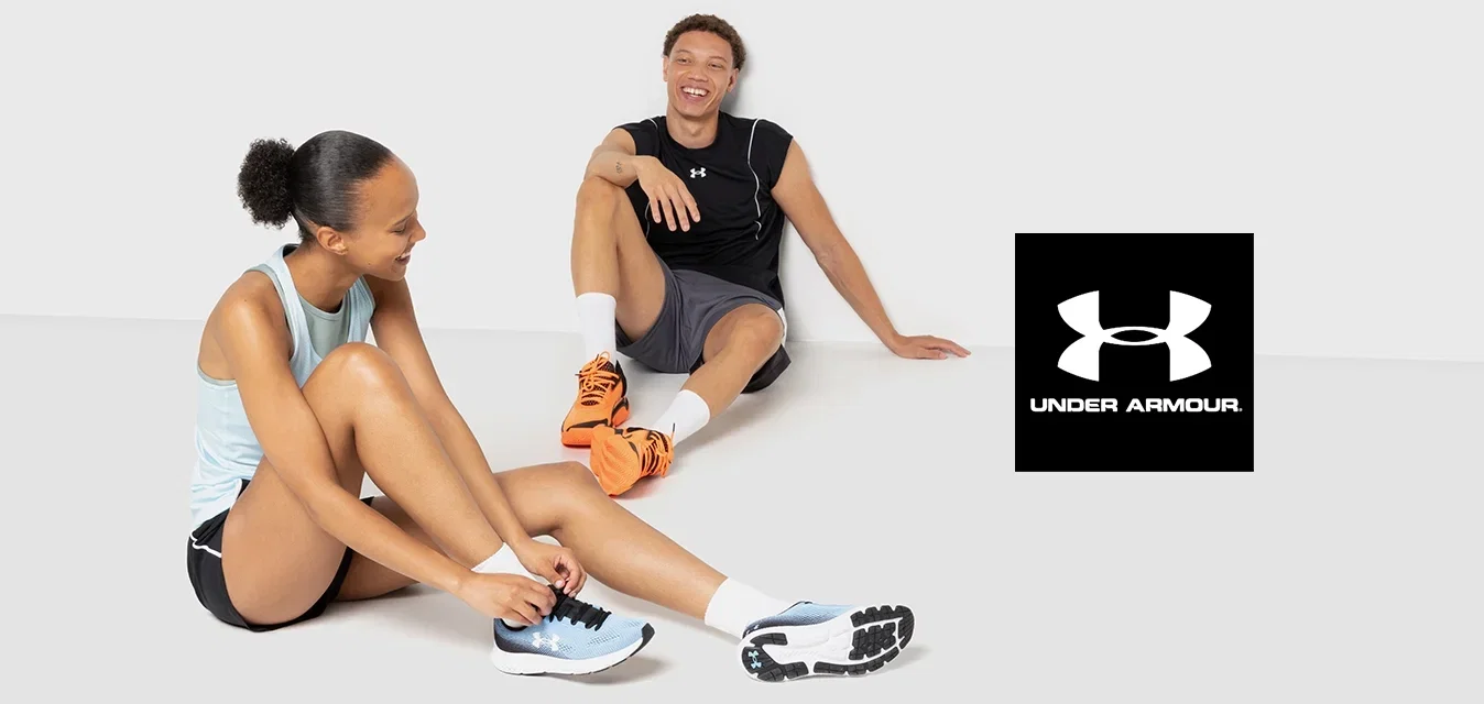 Twee personen in sportkleding zitten op een gladde, lichte achtergrond. De één draagt een lichtblauw tanktop, zwarte shorts en blauwe hardloopschoenen. De ander heeft een zwart mouwloos shirt aan, grijze shorts en oranje hardloopschoenen.