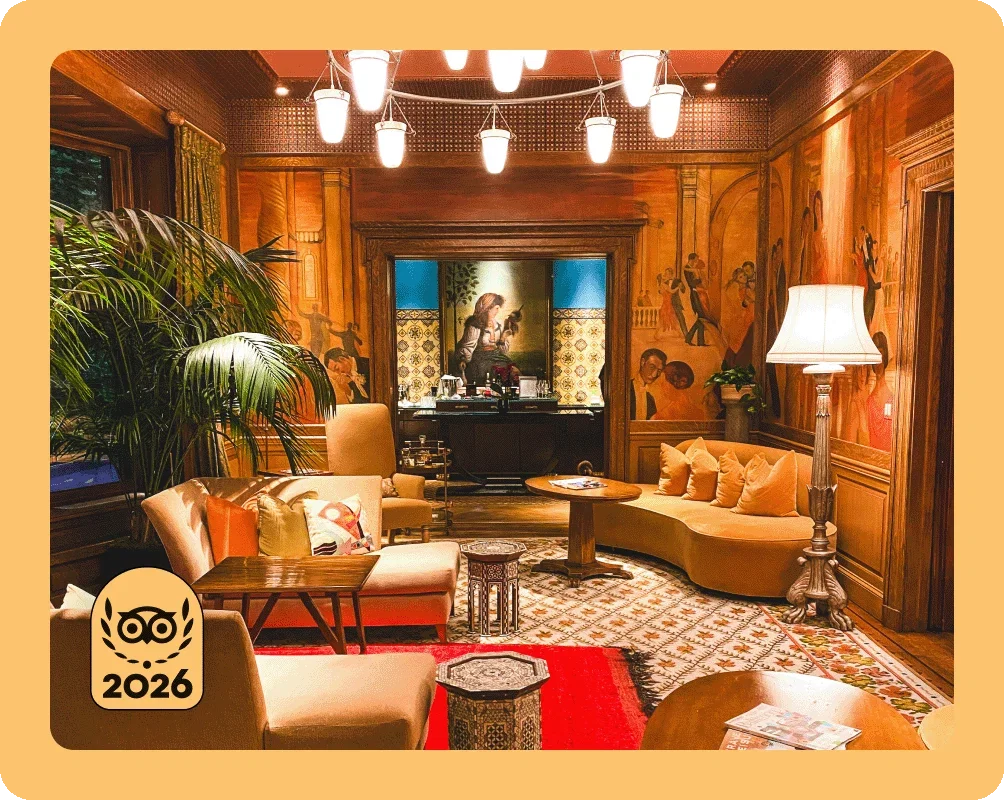 Image Description: A hotel lobby with orange velvet couches and green palm trees. A gold 2026 Travelers’ Choice Best of the Best badge is on the bottom left corner of the image.