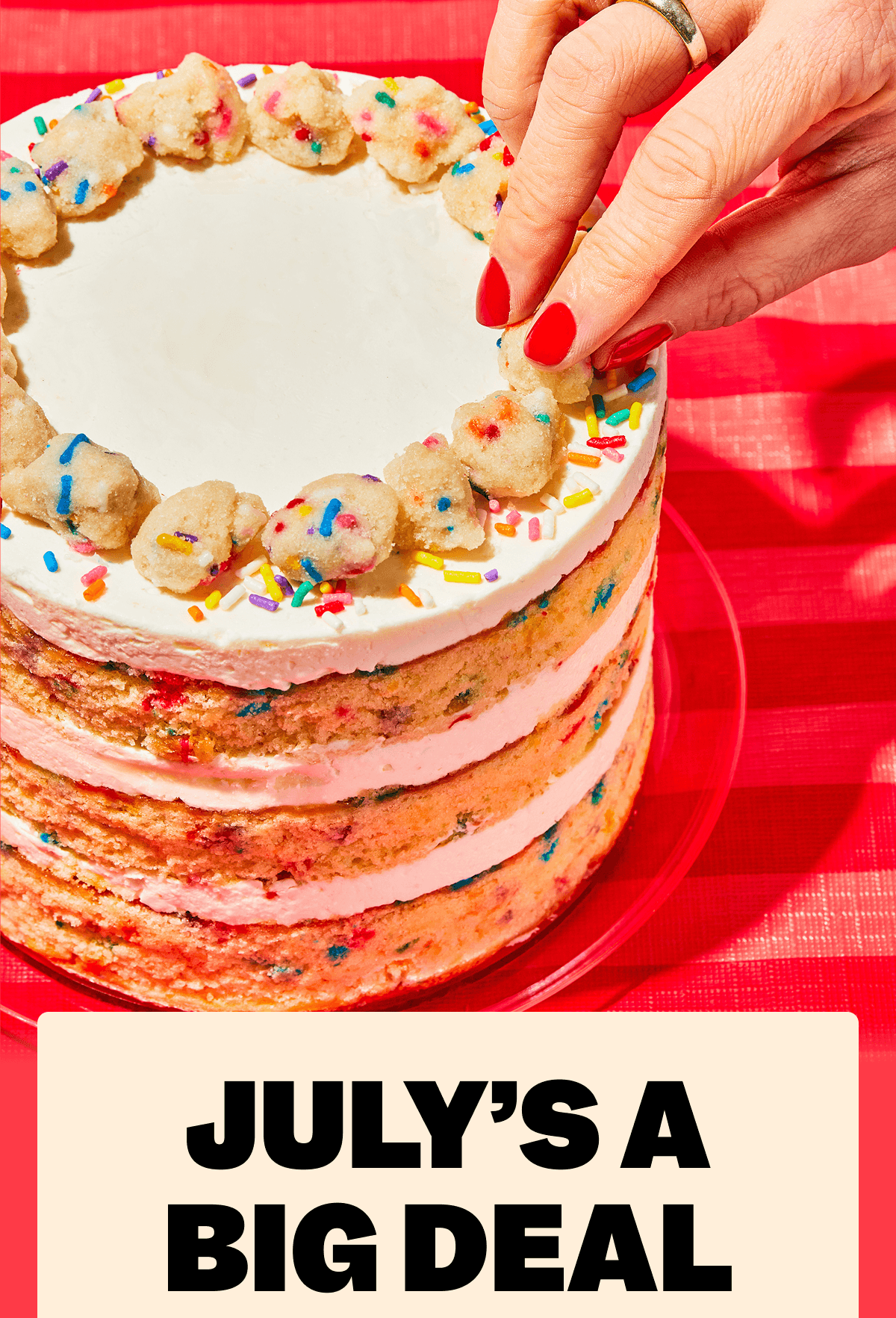 Close-up of a hand placing cake crumbs on a sprinkle layer cake on a red striped tablecloth. Text reads: JULY’S A BIG DEAL.