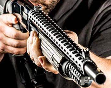 A man holds a pump-action shotgun up to his shoulder, preparing to fire.