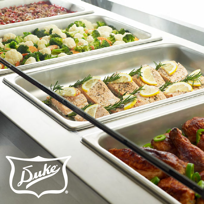 Duke hot food table holding prepared entrées, vegetables, and sides in stainless steel pans within a buffet service line.