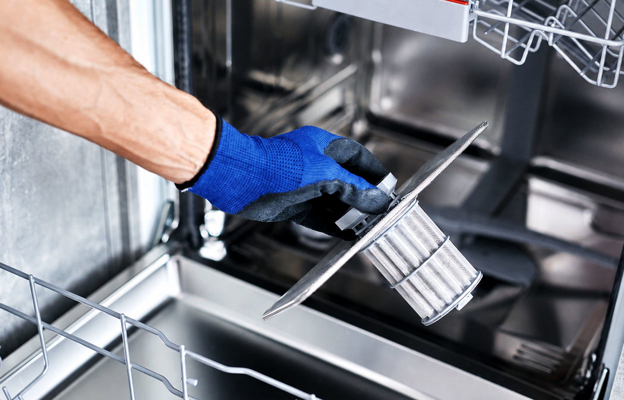 A person cleaning out the filter of a dishwasher