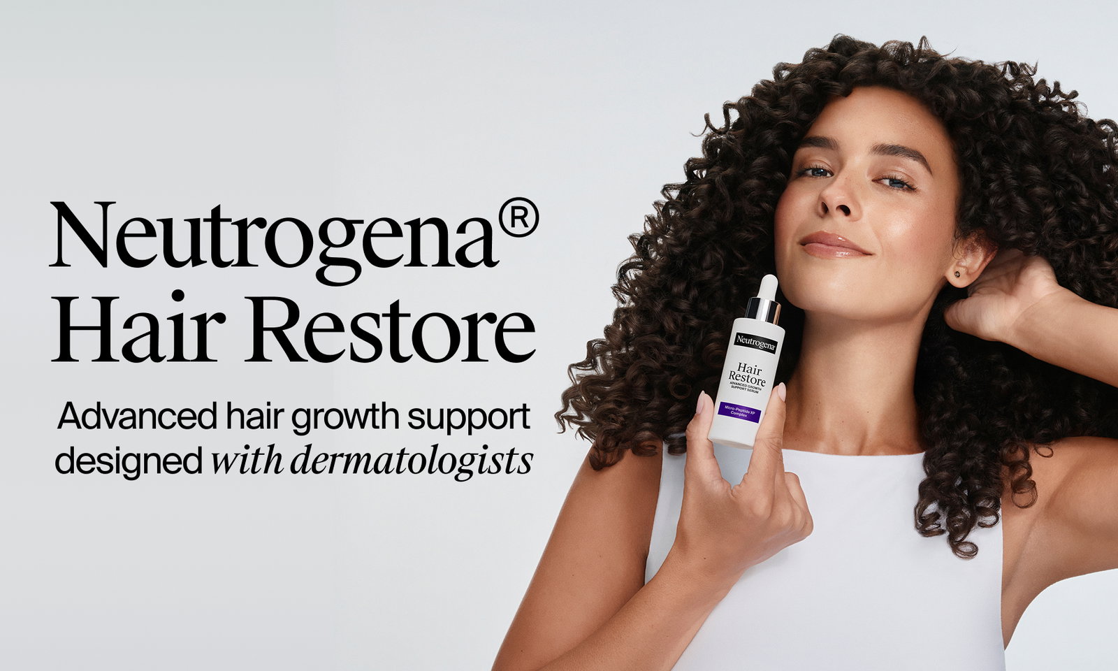 Woman with curly hair holding bottle of Neutrogena® Hair Restore Support Serum