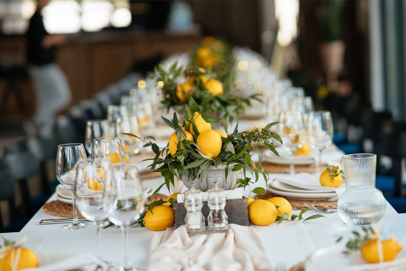 Long summer dining table with white linens, lemon centerpieces and green foliage