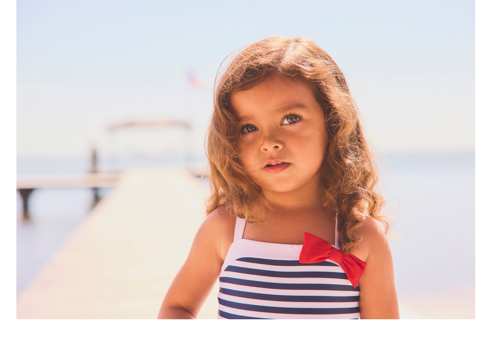 Young girl in navy striped swimsuit with red bow on a sunny pier