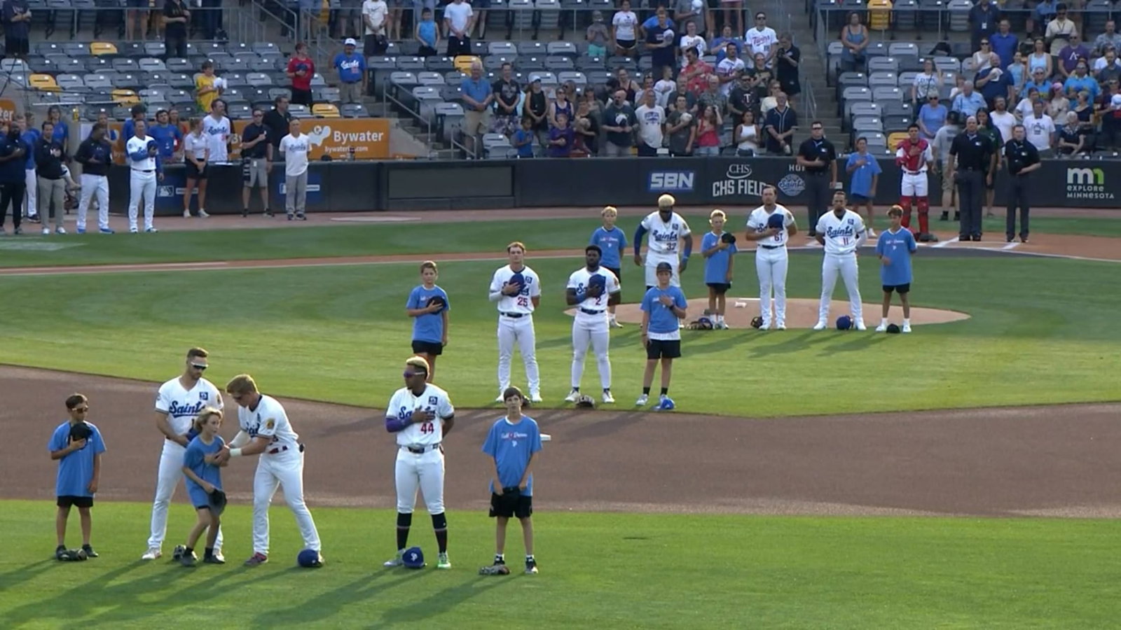 As players stand for the national anthem, one reaches over to support a child struggling in the heat
